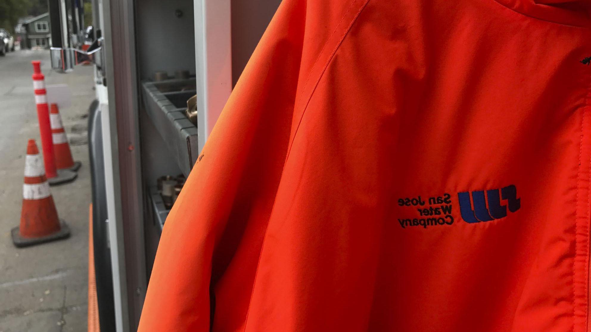 Orange jacket with SJW logo in foreground and pylons in the background